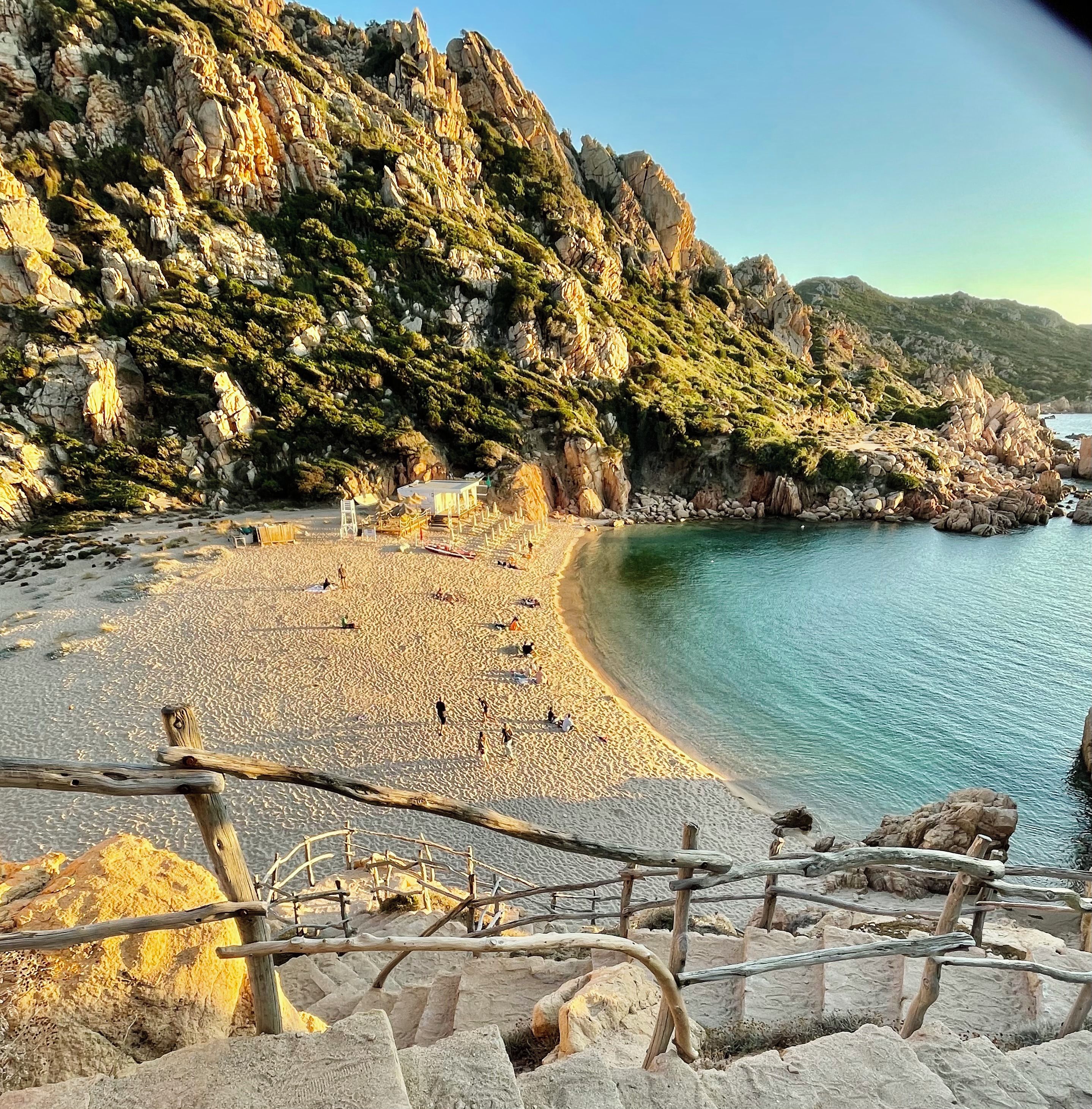 Une plage côtière bordée de falaises rocheuses, avec une étendue de sable et une mer bleue et limpide.