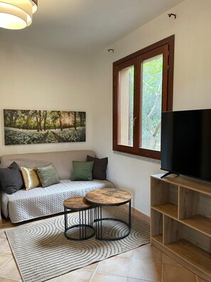 Ein Wohnzimmer mit einer Couch, einem Gemälde, einem Fernseher, einem Fenster und einem Teppich.