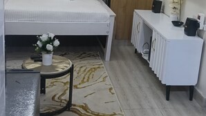 A bedroom with a bed, a white bedside table, a TV, and a small table with a vase of flowers. - Cozy Airbnb Studio with lift ,Parking, Security 24hrs near JKIA (Nairobi)