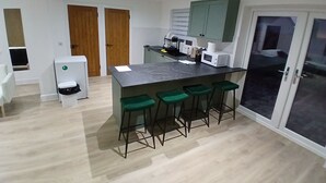 Una cocina moderna con encimera de mármol, taburetes de bar verdes, microondas y refrigerador.