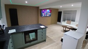 Una cocina moderna con encimera negra, panel de pared de madera y un televisor de pantalla plana montado encima.