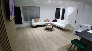 Een moderne woonkamer met een witte bank, een salontafel en een bar met krukken.