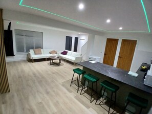 Un saló modern amb un sofà blanc, una taula de centre i una zona de bar amb tamborets.