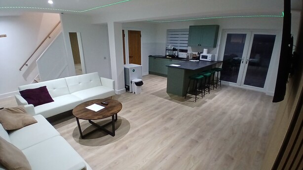 Una sala de estar moderna con un sofá blanco, una mesa de centro y una zona de cocina con barra y taburetes.