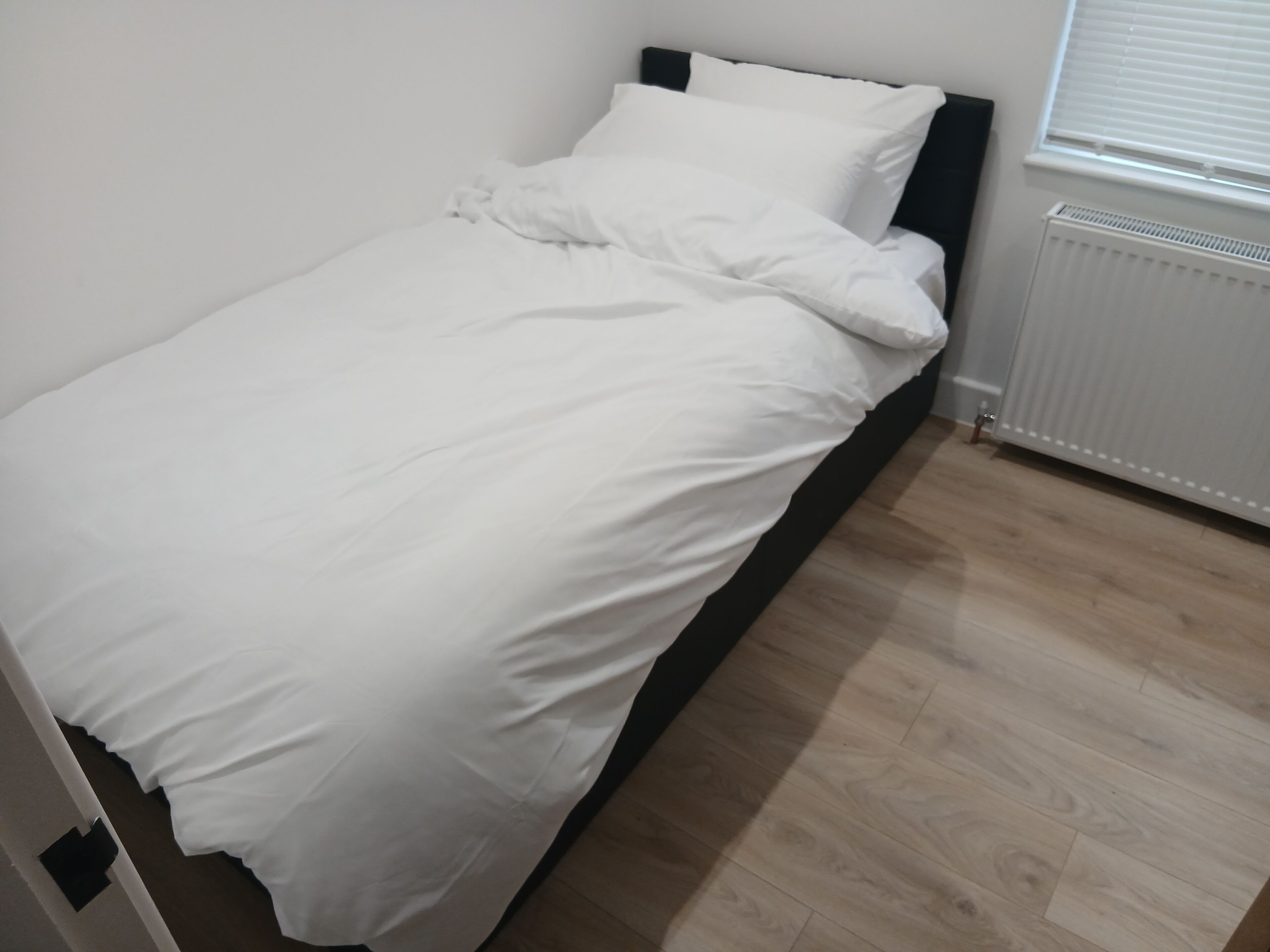 A single bed with white bedding in a room with wooden flooring and a white radiator.