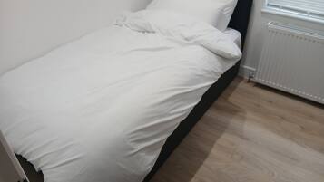 A single bed with white bedding in a room with wooden flooring and a white radiator.