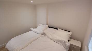 A bedroom with a bed, pillows, a nightstand, and a drawer unit.