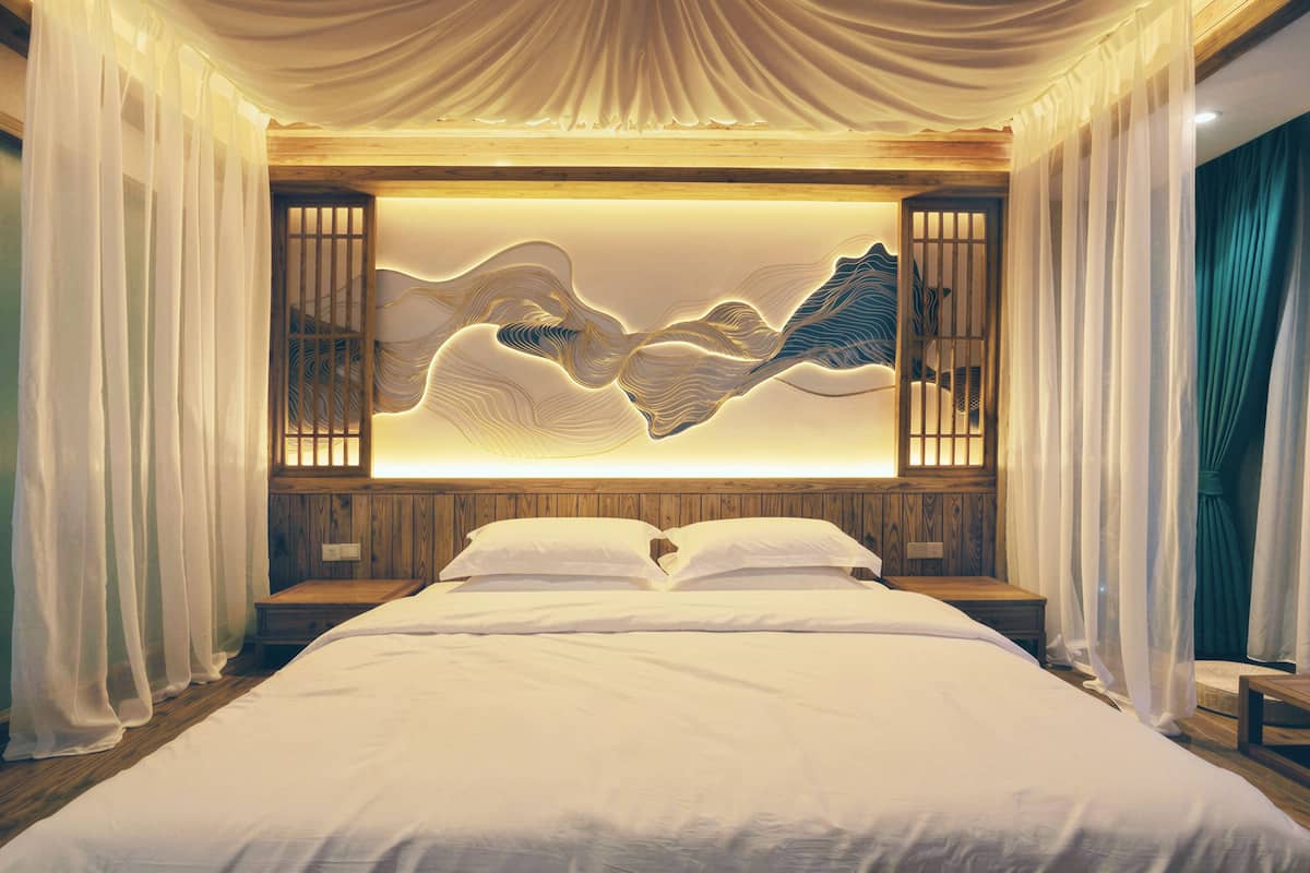 A bedroom with a bed, curtains, and a wall-mounted artwork.