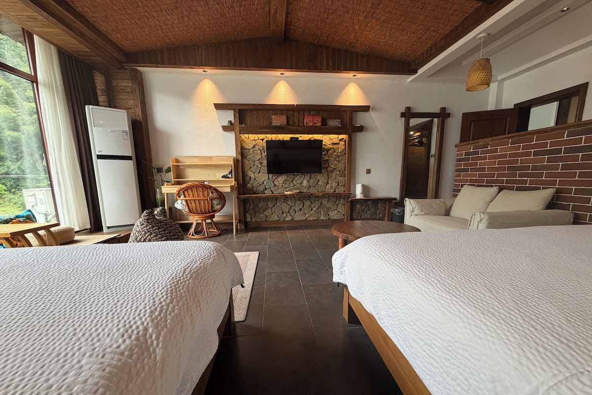 A hotel room with two beds, a stone fireplace, a television, and a wooden ceiling.