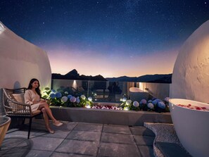 En kvinde sidder i en stol på en balkon med udsigt til nattehimmel og bjerge.