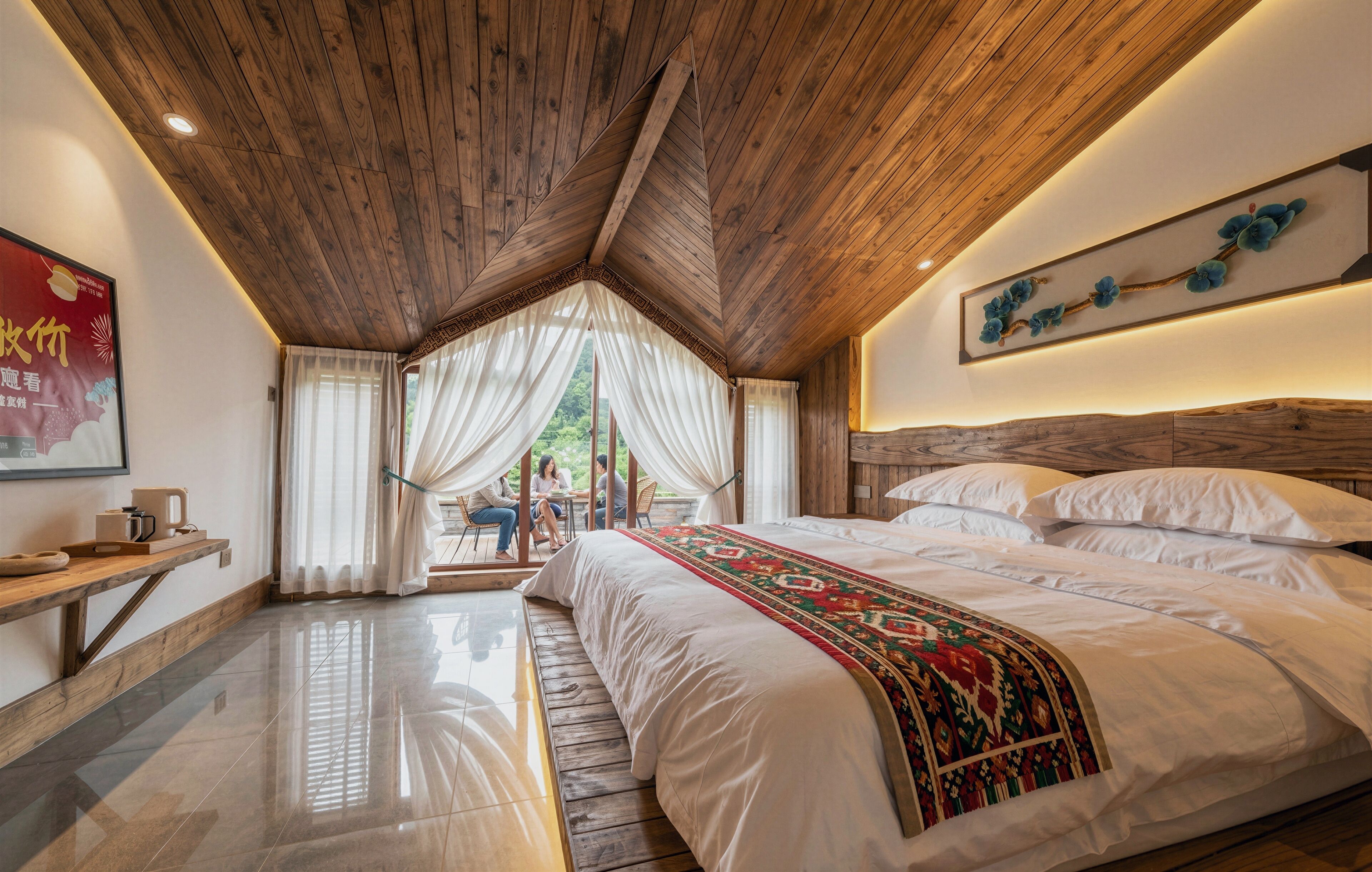 A bedroom with a wooden ceiling, a large bed with a patterned bedspread, a bedside table, and a wall-mounted artwork.