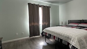A bedroom with a bed, a nightstand, a dresser, and a window with curtains. - Welcoming 4-bedroom house in Anchorage for a relaxing stay (Anchorage)