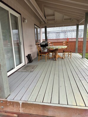 A covered outdoor patio with a table and chairs, a grill, and a sliding glass door.