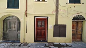 A building with a central wooden door, a metal gate, and a number '42' on the wall. - Hostdomus - Oscar's House (Albenga)