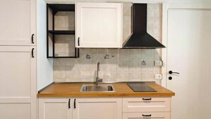 A kitchen with white cabinets, a black range hood, a stainless steel sink, and a wooden countertop. - Hostdomus - Oscar's House (Albenga)