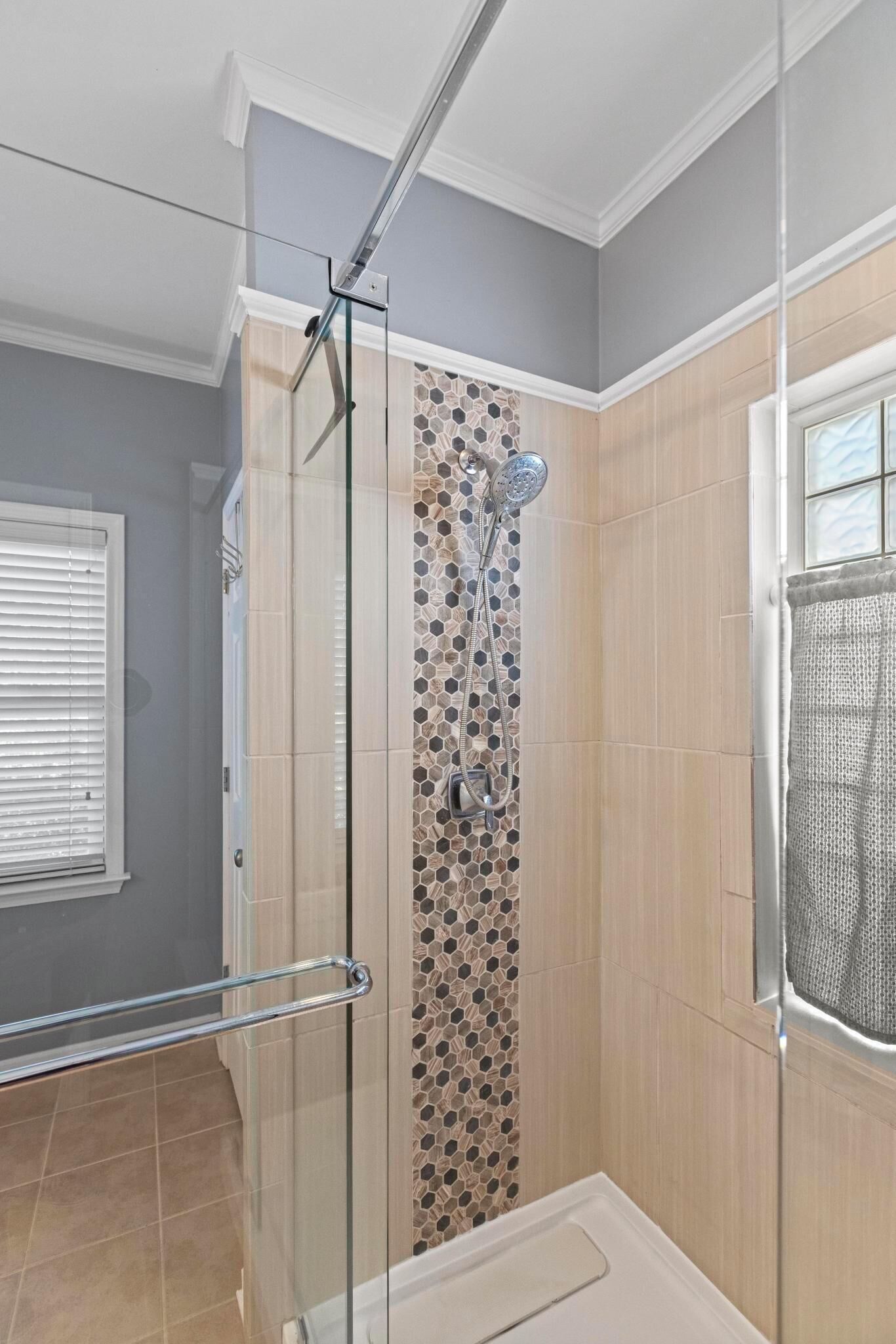 A glass-enclosed shower with a tiled wall, a showerhead, and a handrail.