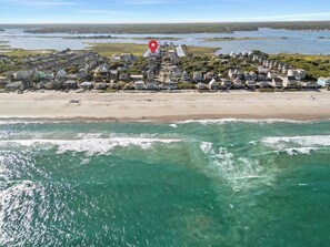 Luftaufnahme einer Küstenwohngegend mit Häusern direkt am Strand, blauem Himmel und ruhiger See.