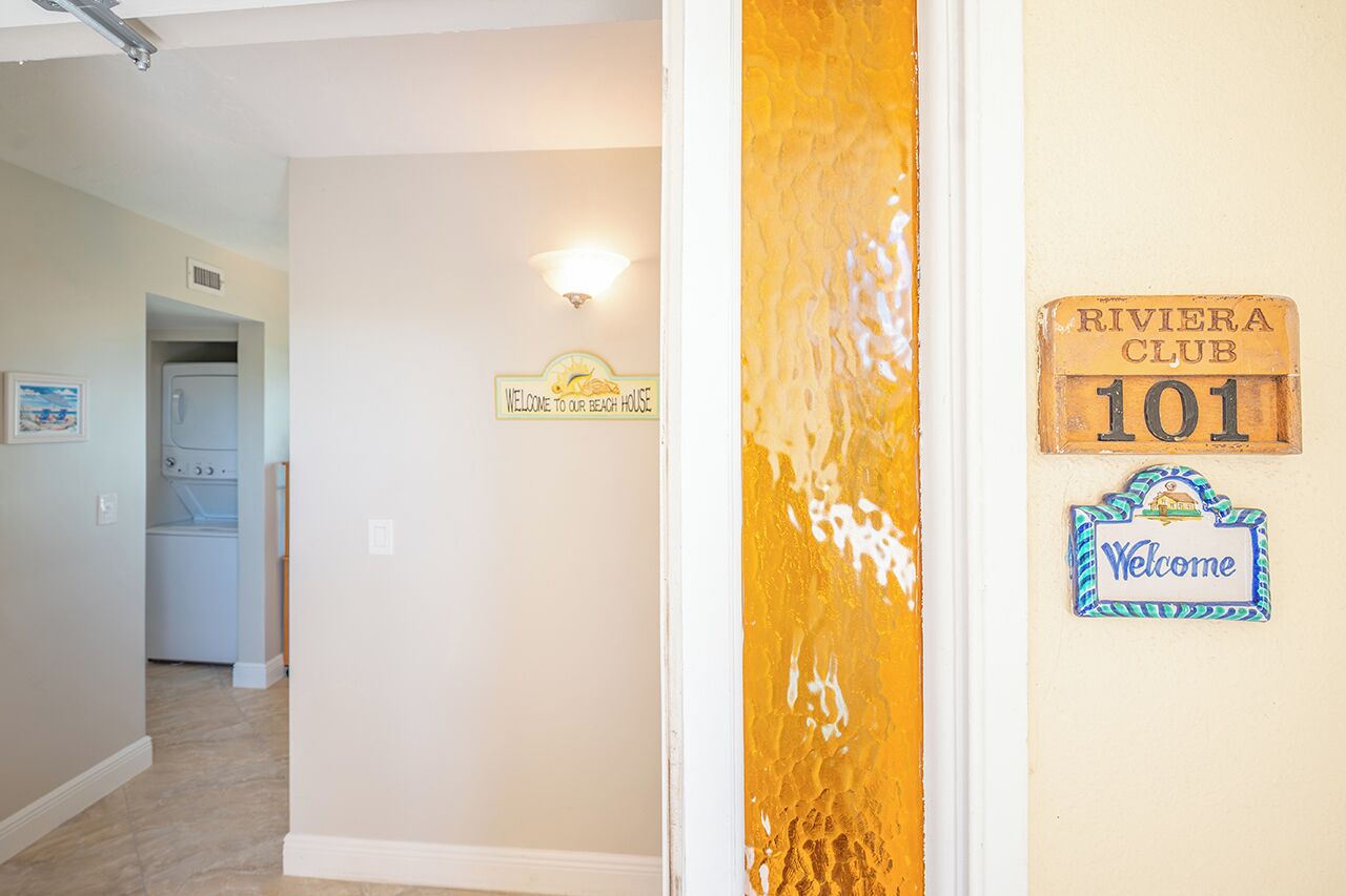 A hallway with a laundry room, a welcome sign, and a Riviera Club sign.