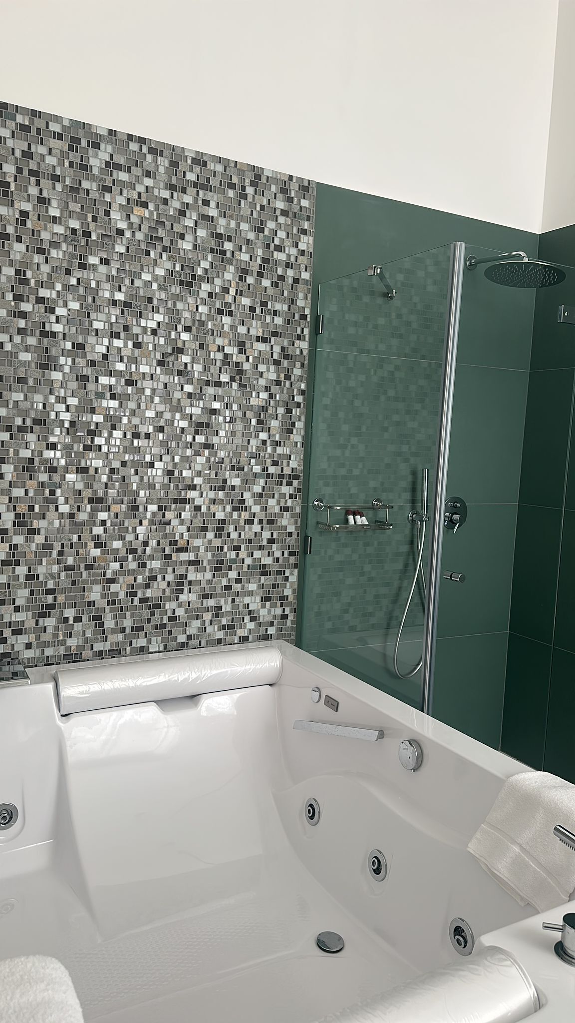 A modern bathroom with a mosaic tile wall, a glass-enclosed shower, and a white bathtub with a built-in seat.