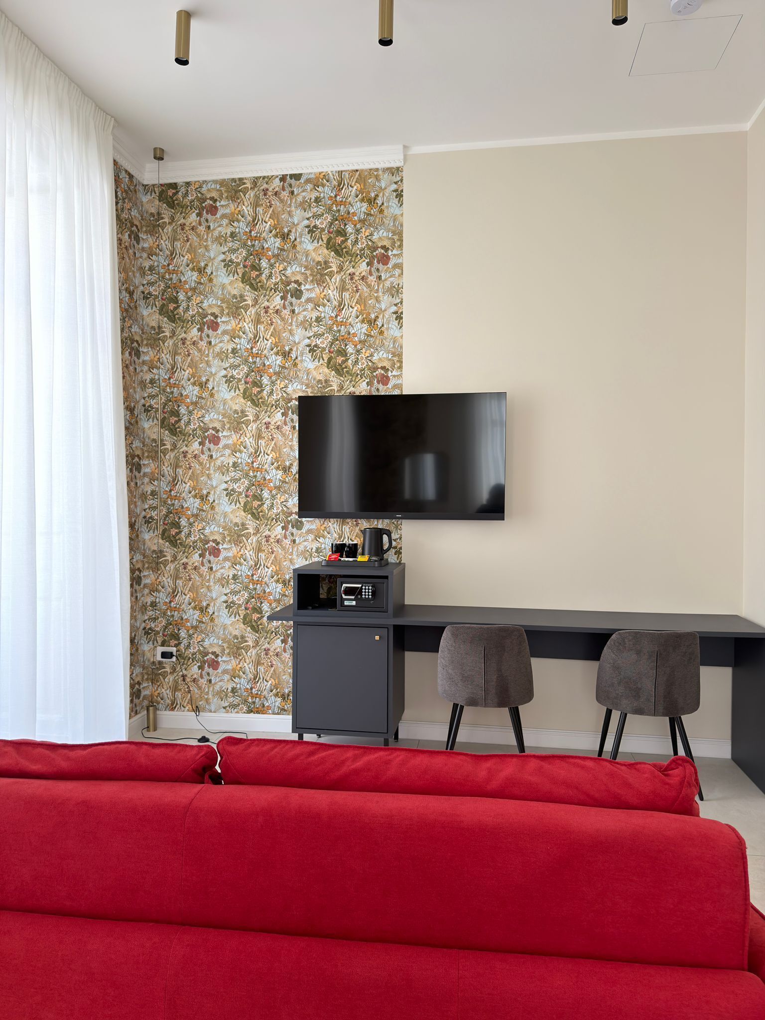A modern living room with a sofa, a TV mounted on the wall, a small cabinet, and two chairs.