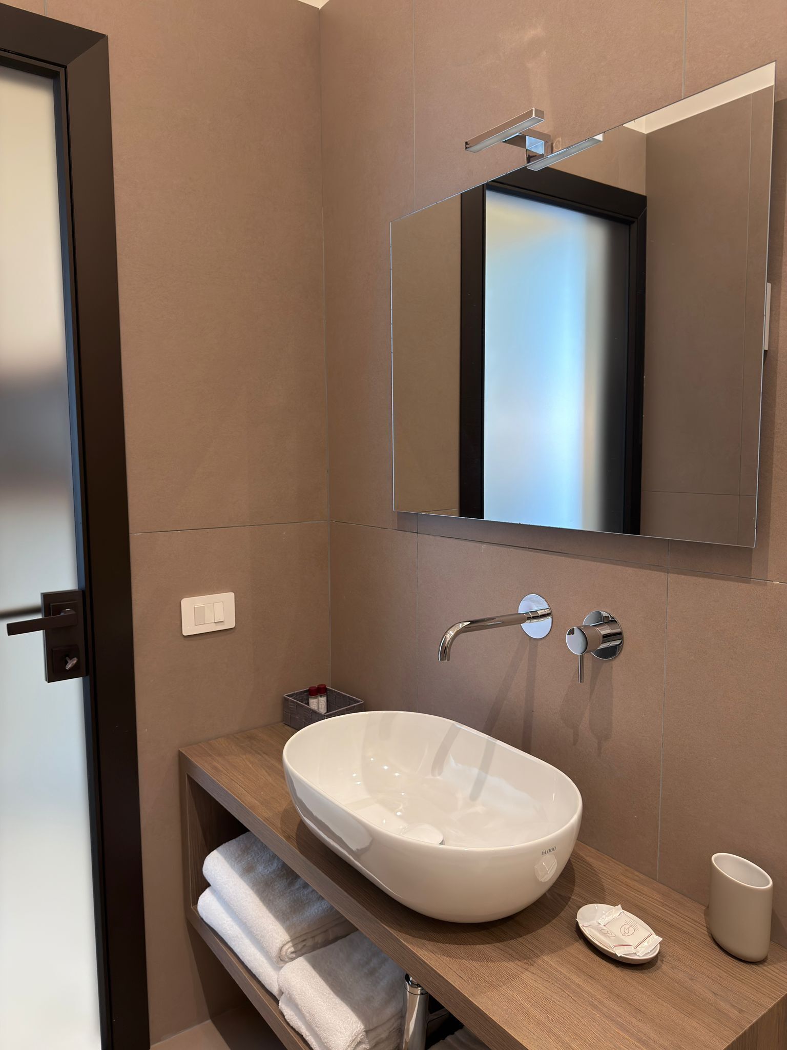 Une salle de bain moderne avec un grand lavabo ovale, un miroir, un porte-serviettes et un gobelet.