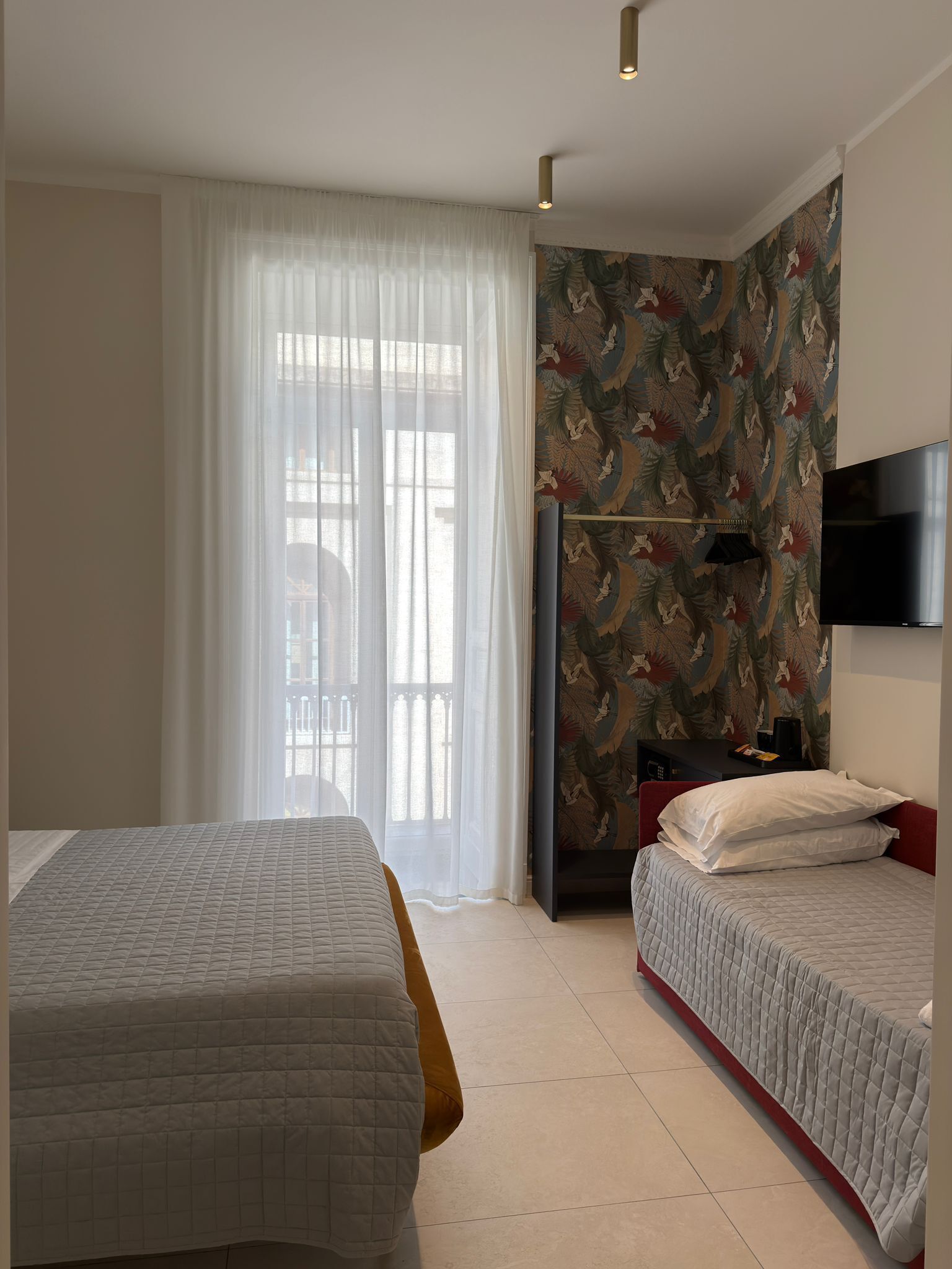Een hotelkamer met twee bedden, een televisie en een raam met dunne gordijnen.