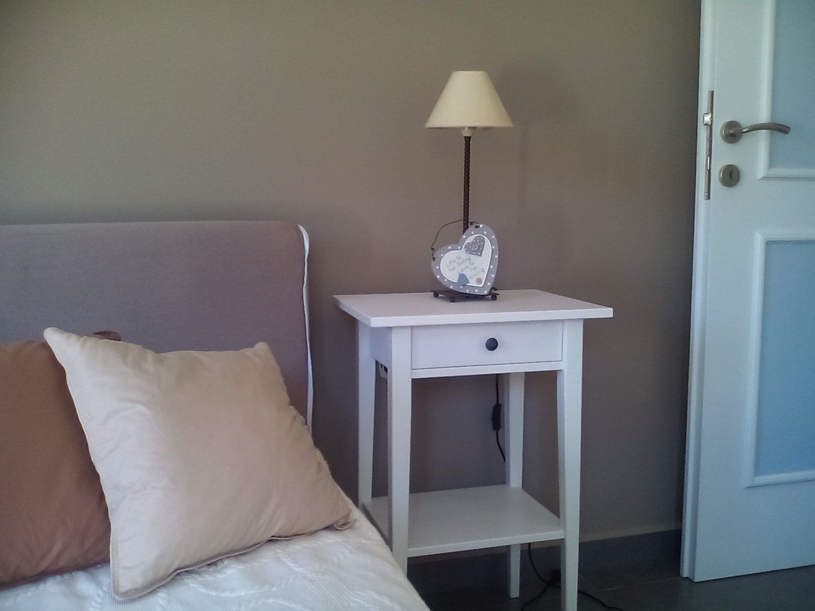 A bed with pillows, a bedside table with a lamp, and a door.