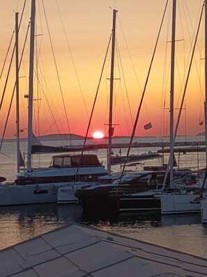 Ein Yachthafen mit mehreren Segelbooten, ein klarer Himmel und ein Sonnenuntergang im Hintergrund.