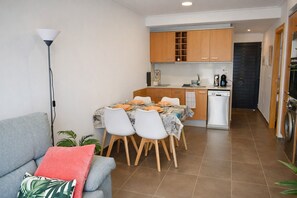 A compact living space with a dining area, kitchenette, and a sofa with a red cushion. - Anacasa Dunas MET Oliva Nova AP224 (Oliva)