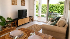 Een woonkamer met een televisie, houten meubels, een schuifpui naar een terras en een bordje met de tekst 'Welcome Beach House'.