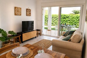 Ein Wohnzimmer mit Fernseher, Holzmöbeln, einer Schiebetür zu einer Terrasse und einem Schild mit der Aufschrift 'Welcome Beach House'.