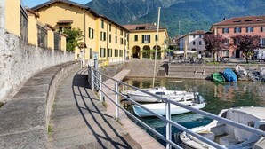 Une zone riveraine où des bateaux sont amarrés, des bâtiments dotés de balcons, et une montagne en arrière-plan.