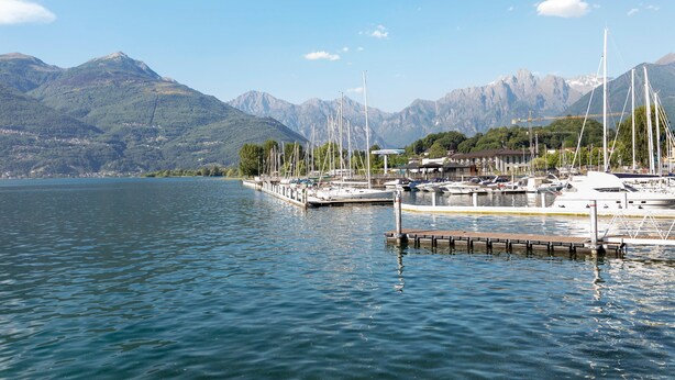 Un port de plaisance avec des bateaux amarrés, un quai et des montagnes en arrière-plan.