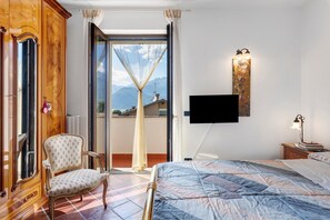 Ein Schlafzimmer mit einem Bett, einem Sessel, einem Fernseher und Blick auf Berge durch eine Schiebetür.