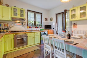 Cuina amb armaris verdosos, fogó, forn i zona de dinar amb taula preparada per a dues persones.