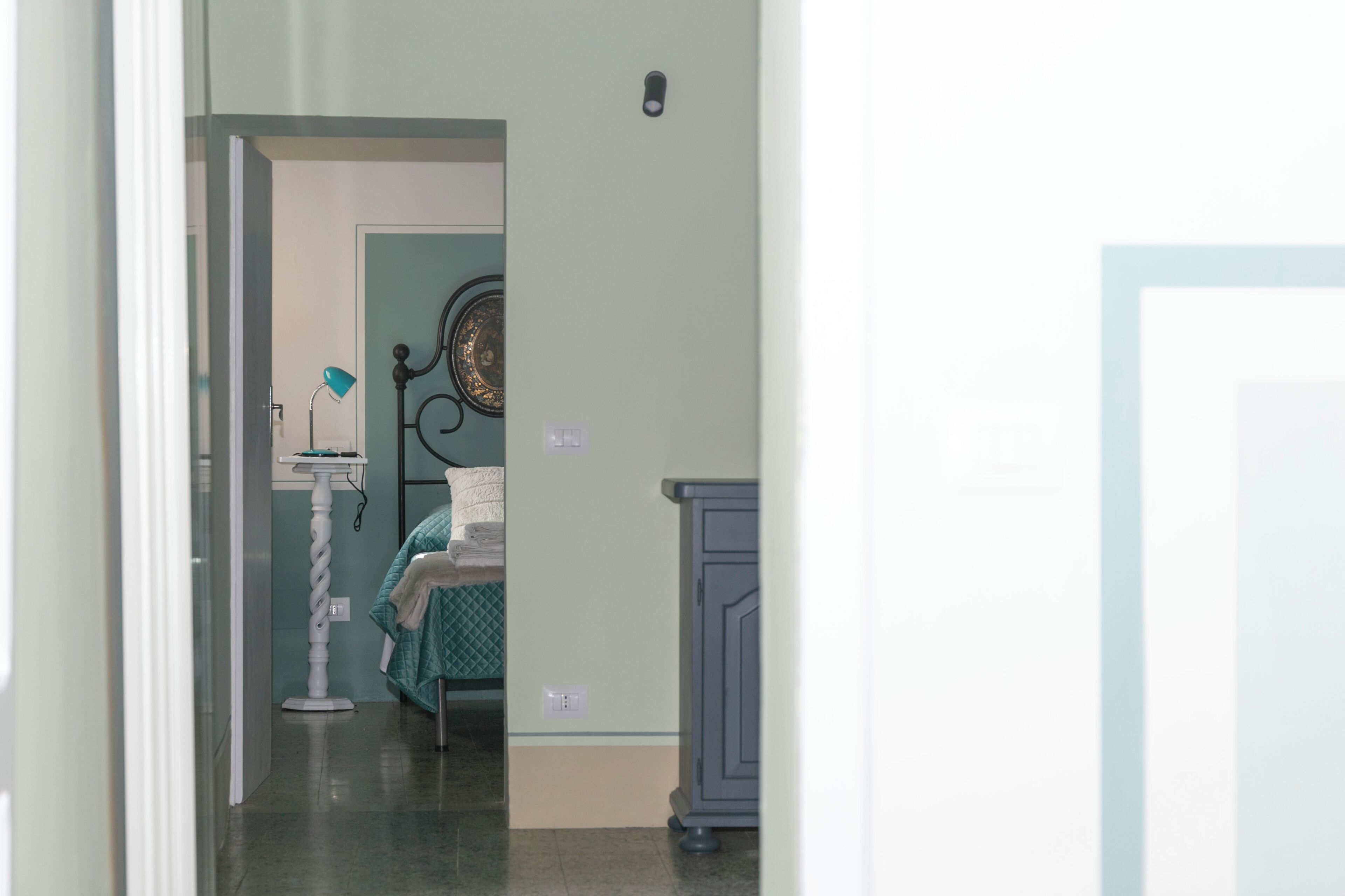 Un pasillo estrecho que conduce a una habitación con una cama, una mesita de noche y un adorno en la pared.