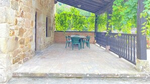 Um edifício de pedra com varanda coberta, apresentando uma mesa e cadeiras.