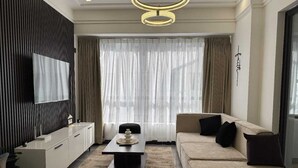 A modern living room with a sofa, a coffee table, a TV mounted on the wall, and a large window with curtains. - Urban stays (Nairobi)