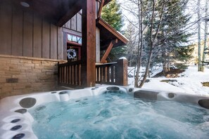 Ein Whirlpool vor einer Holzhütte mit einer Steinwand, einer Holzterrasse und verschneitem Boden.