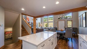 Une cuisine spacieuse dotée d’un îlot central, de planchers en bois et de grandes fenêtres offrant une vue sur l’extérieur.
