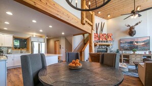 Un vaste espace de vie comprenant une table ronde en bois, des fauteuils à revêtement gris, une cheminée et une tête de cerf fixée au mur.
