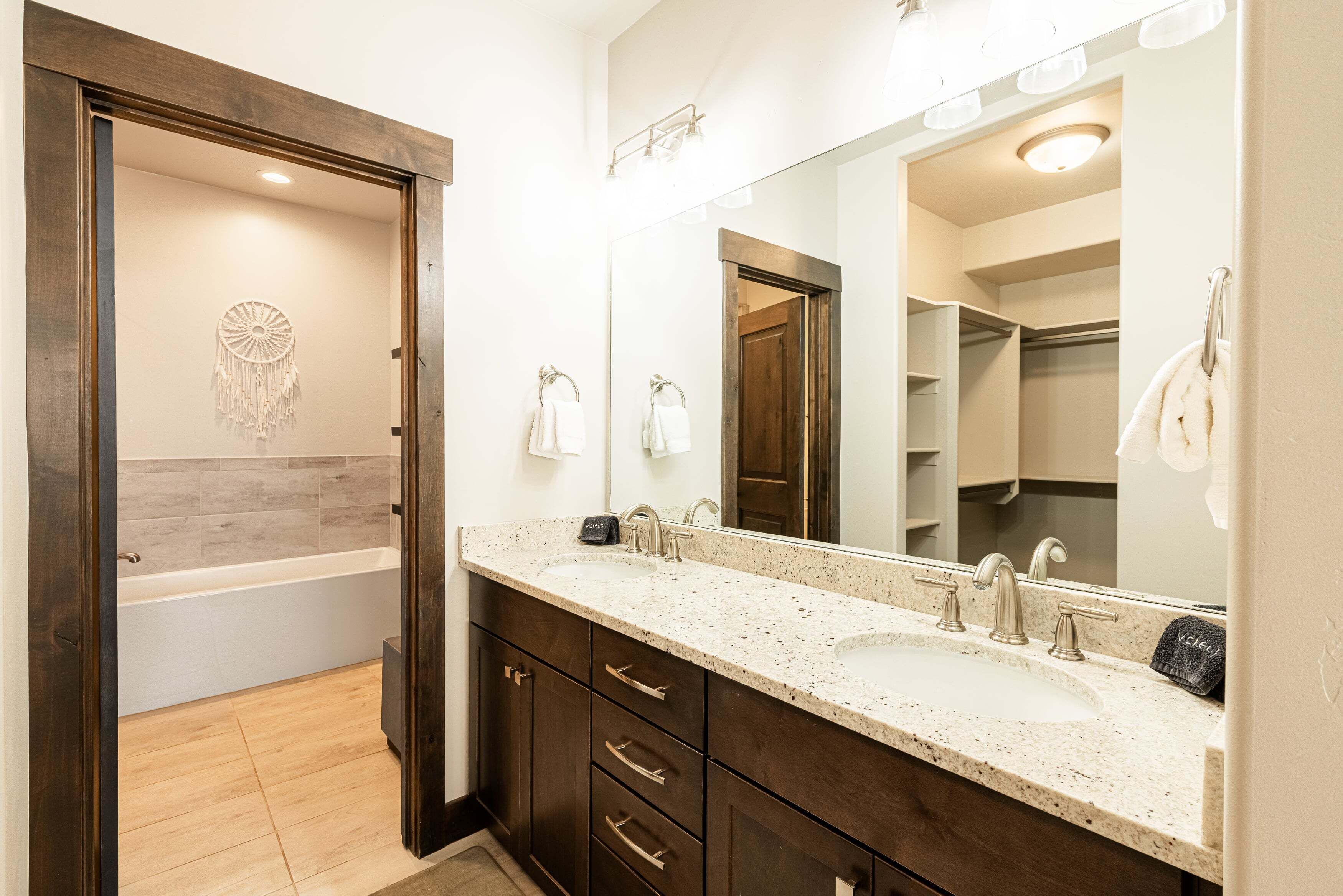A bathroom with a bathtub, two sinks, a vanity with drawers, a large mirror, and a dreamcatcher decoration.