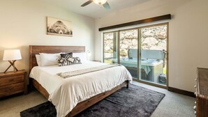 Quarto com cama, mesa de cabeceira, ventoinha no teto, janela com vista e porta deslizante para área externa.