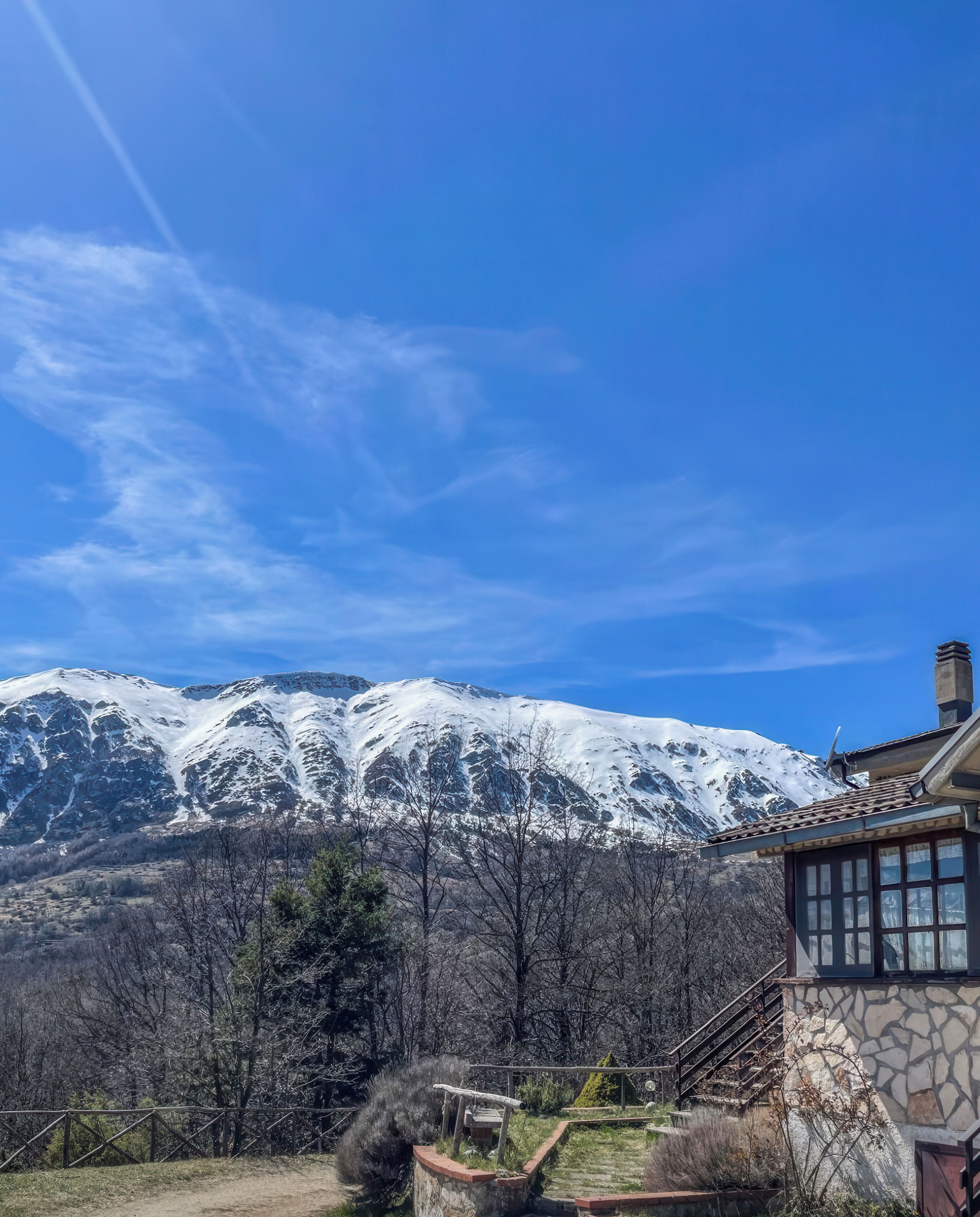 A mountainous landscape with a house featuring a stone wall and a wooden staircase.