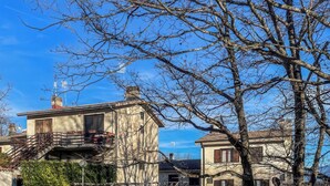 Ein traditionelles Steinhaus mit einer Treppe, die zu einem Balkon führt, umgeben von kahl stehenden Bäumen und einem klaren Himmel.