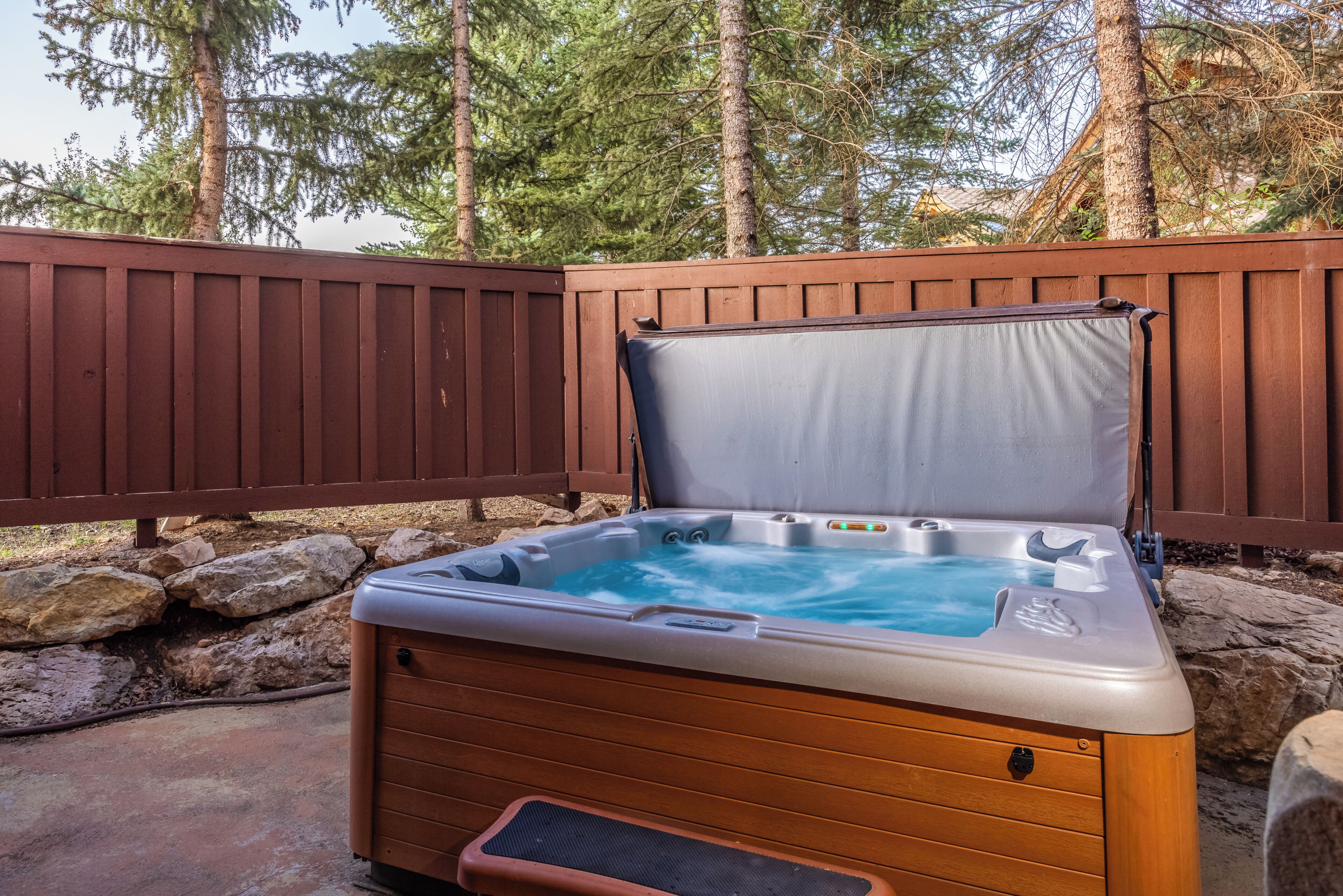 A hot tub with a wooden exterior and a metal frame, surrounded by a wooden fence and a stone wall.