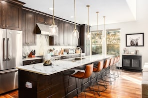 A modern kitchen with dark wood cabinets, a marble island, bar stools, stainless steel appliances, and pendant lighting. - Spacious 4BR, 4.5BA retreat in Deer Valley with stunning mountain views. (Hideout)