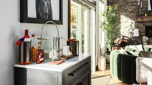 Ein modernes Wohnzimmer mit Kamin, einem grünen Sofa und einer Küchenzeile mit Flaschen und einem Wasserkocher.