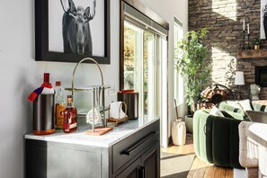 A modern living room with a fireplace, a green sofa, and a kitchen counter with bottles and a kettle. - Spacious 4BR, 4.5BA retreat in Deer Valley with stunning mountain views. (Hideout)