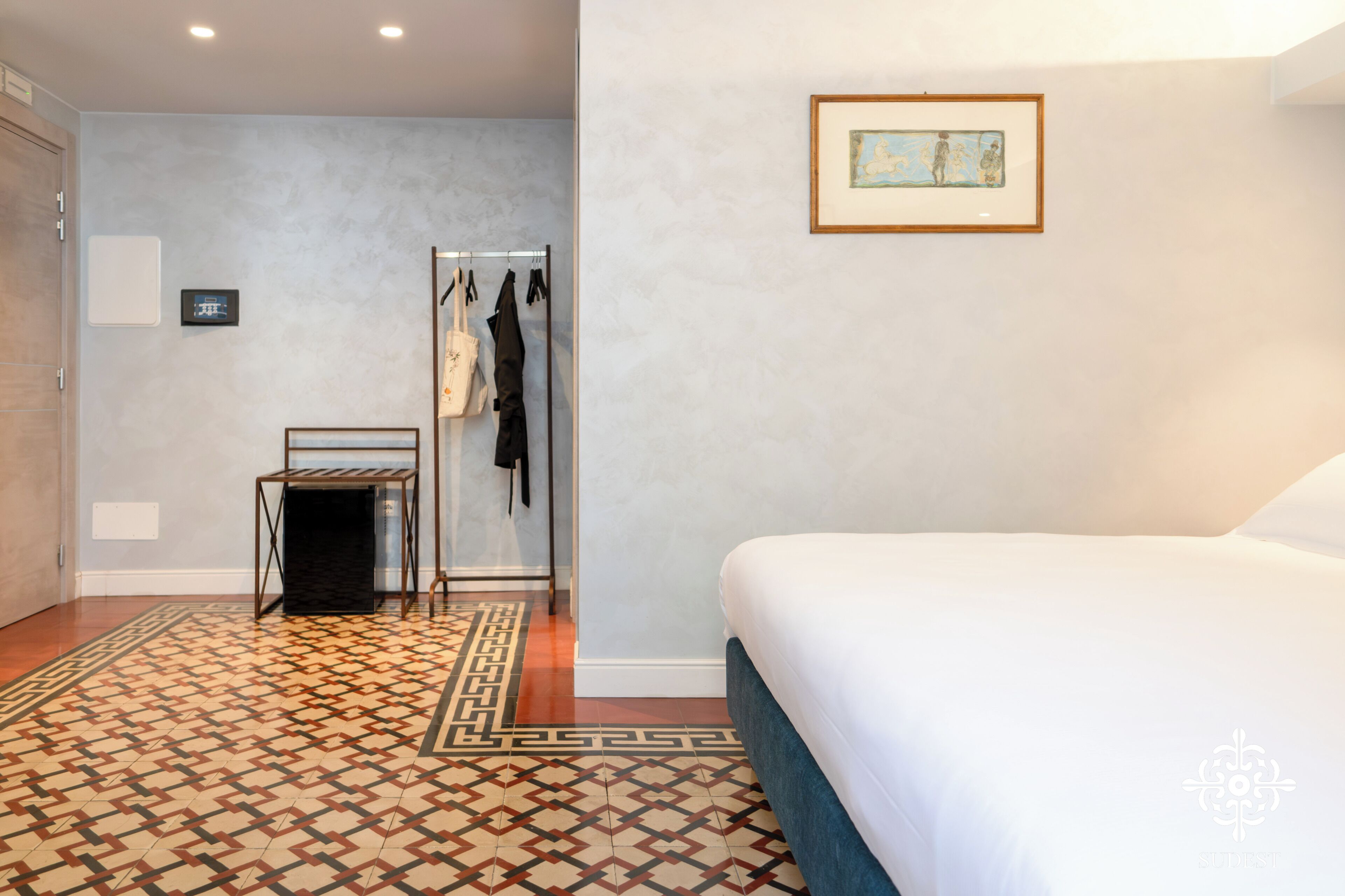 A bedroom with a bed, a wardrobe, a coat rack, and a framed picture on the wall.